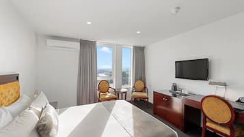 Habitación de hotel con cama, dos sillas, escritorio, televisor y ventana con cortinas.