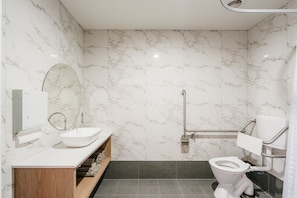 A modern bathroom with a marble wall, a white sink, a mirror, a toilet, and a shower area. - Areca Launceston (Launceston)