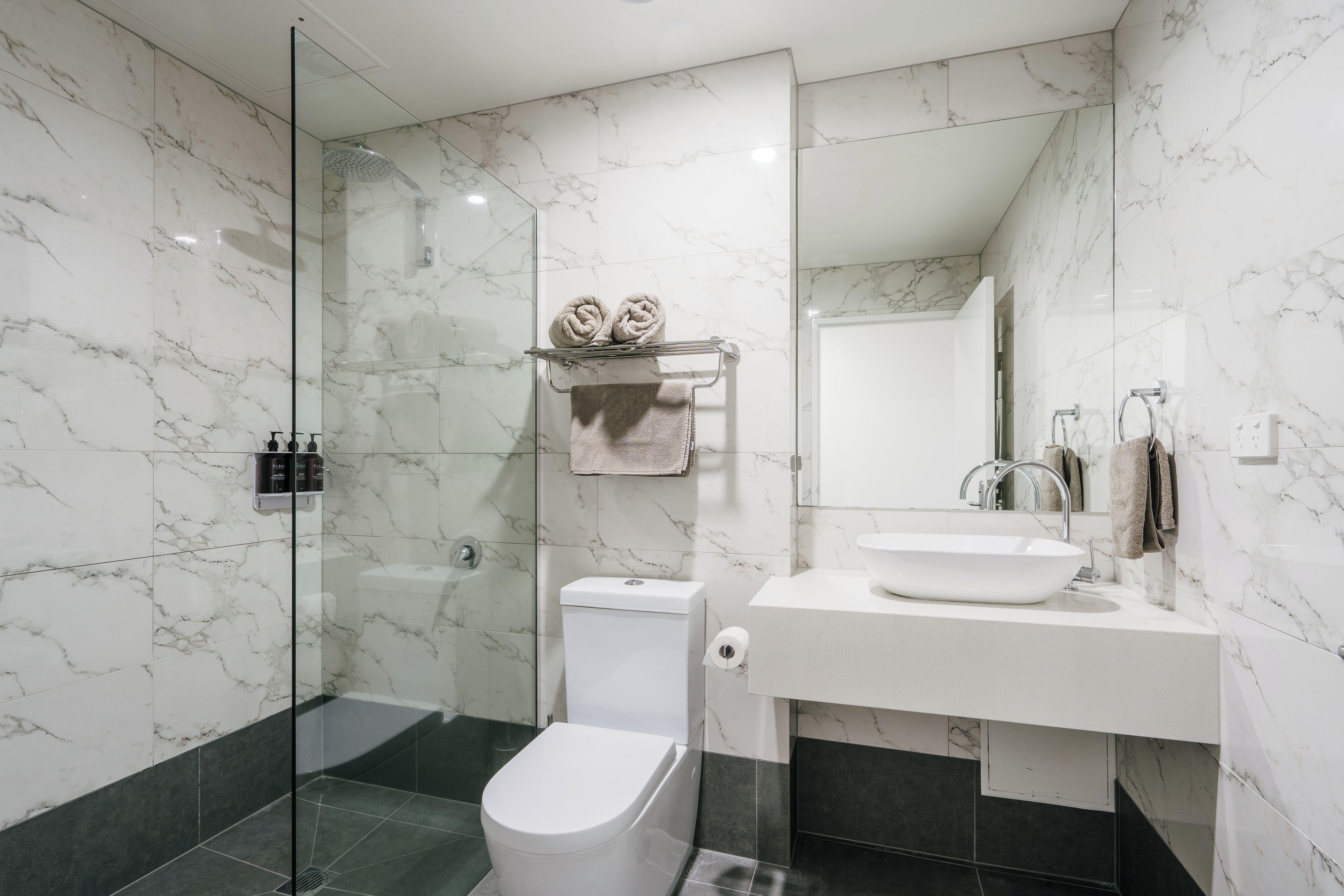 A modern bathroom with a glass shower enclosure, a white toilet, and a sink with a marble countertop.