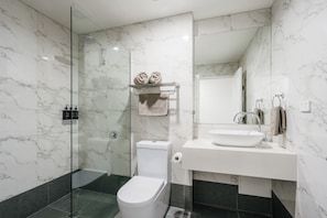 Un baño moderno con cabina de ducha de vidrio, inodoro blanco y lavabo con encimera de mármol.