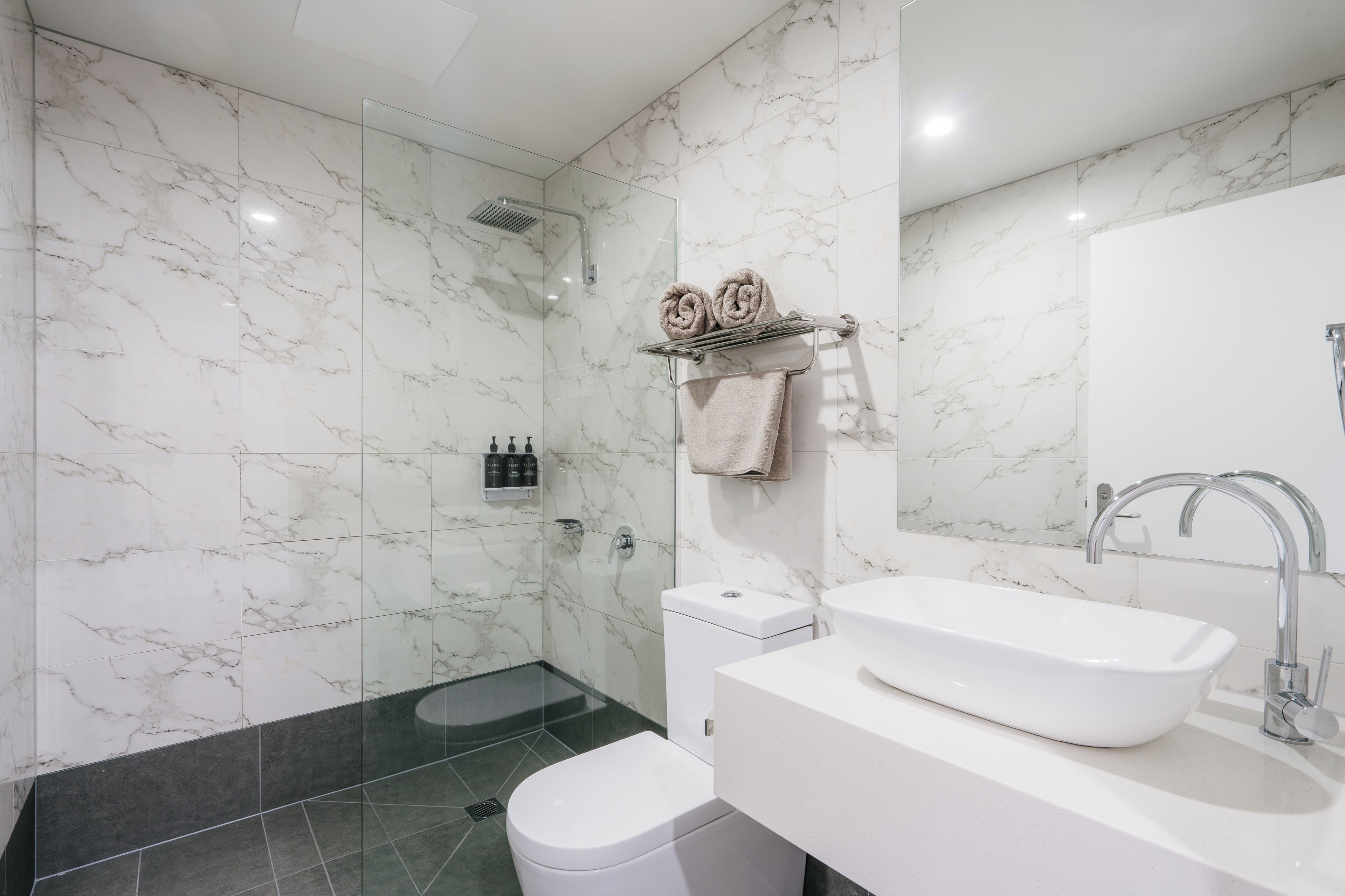 Un baño moderno con cabina de ducha de vidrio, un lavamanos blanco y un inodoro.