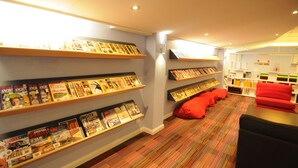 Un hall d’hôtel avec un sol recouvert de moquette, un canapé rouge et des étagères remplies de magazines et de livres.