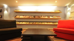 Un salon avec un canapé marron foncé, un canapé rouge et une table basse en bois. On y trouve trois étagères remplies de livres et de magazines.