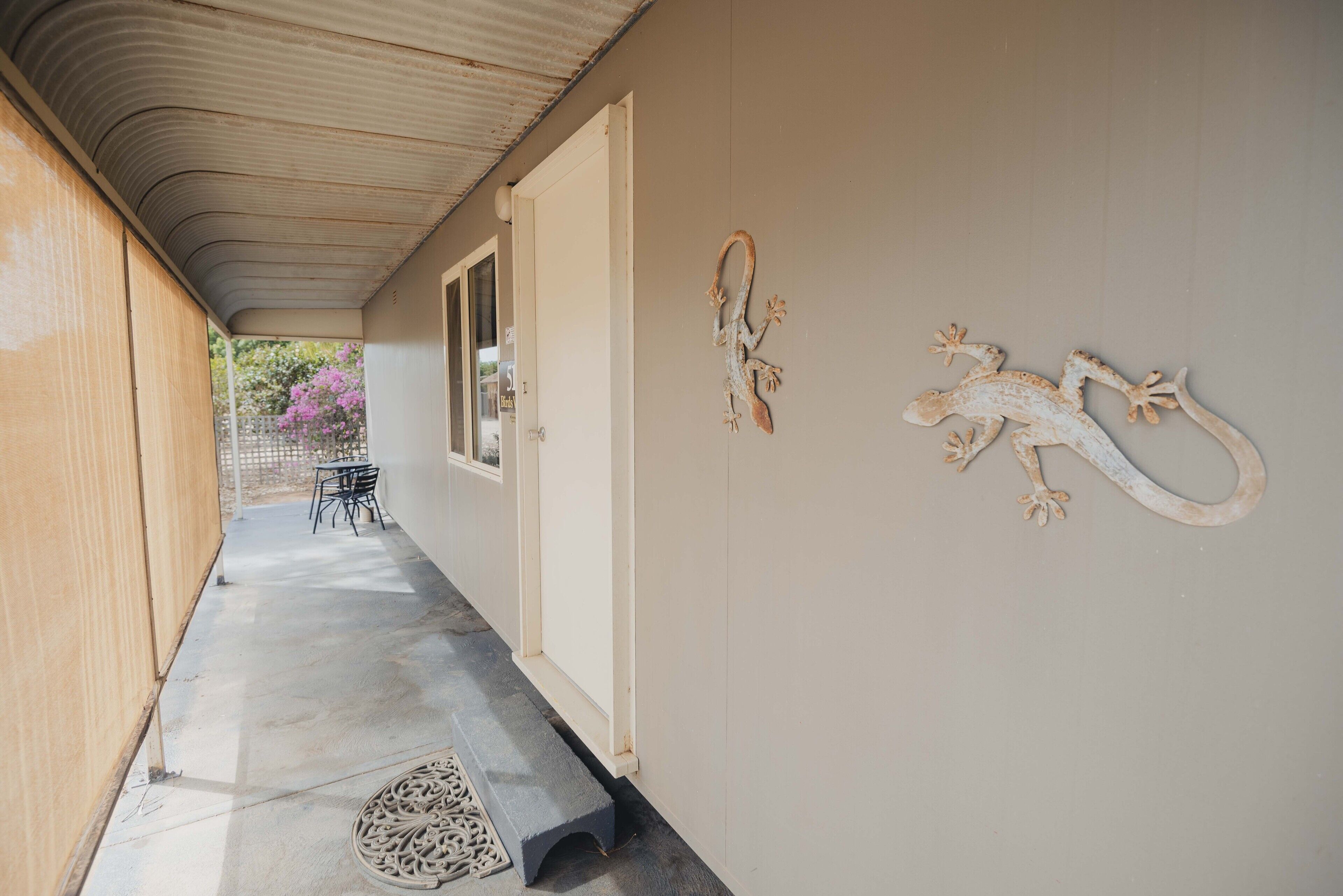 A covered corridor with a bench, a door, and two wall-mounted lizard decorations.