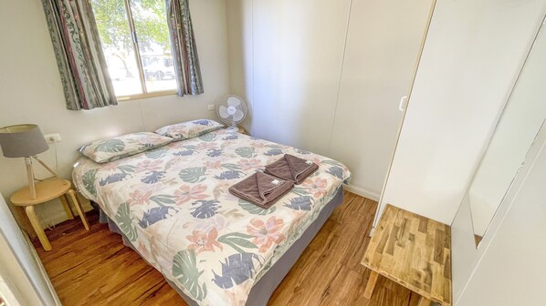 Un dormitorio con colcha estampada, mesita de noche con lámpara y suelo de madera.