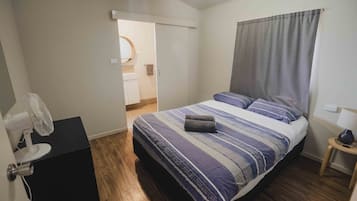 A bedroom with a bed, a fan, a small table, and a door leading to a bathroom.