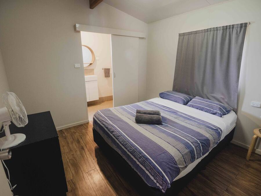 A bedroom with a bed, a fan, a small table, and a door leading to a bathroom.