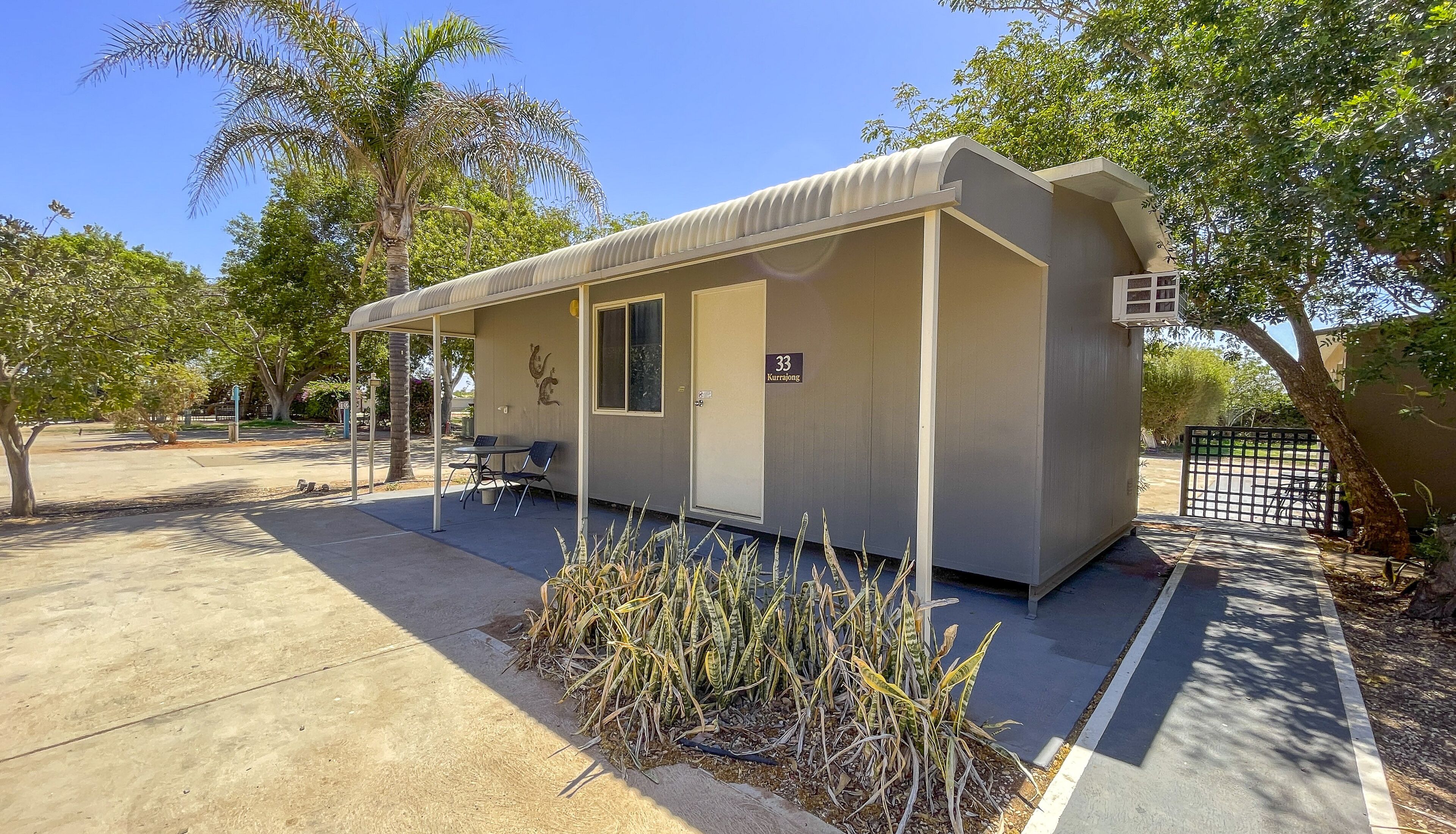 A small, single-story building with a covered patio area, a door labeled "33 Kurrajong," and a parking area with a few parked cars.