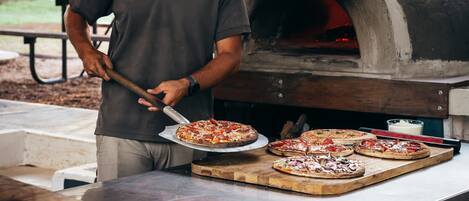 A man in a uniform preparing pizzas at an outdoor brick oven.