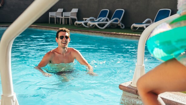 En swimmingpool med en person i vandet og en anden person, der sidder på kanten.