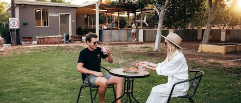 Two people dining at an outdoor table with a view of a building labeled "Camp Kitchen" in the background.