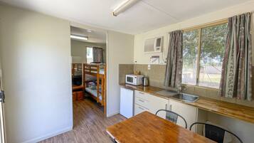 A compact kitchen with a wooden table, a microwave, a sink, and a window with curtains.