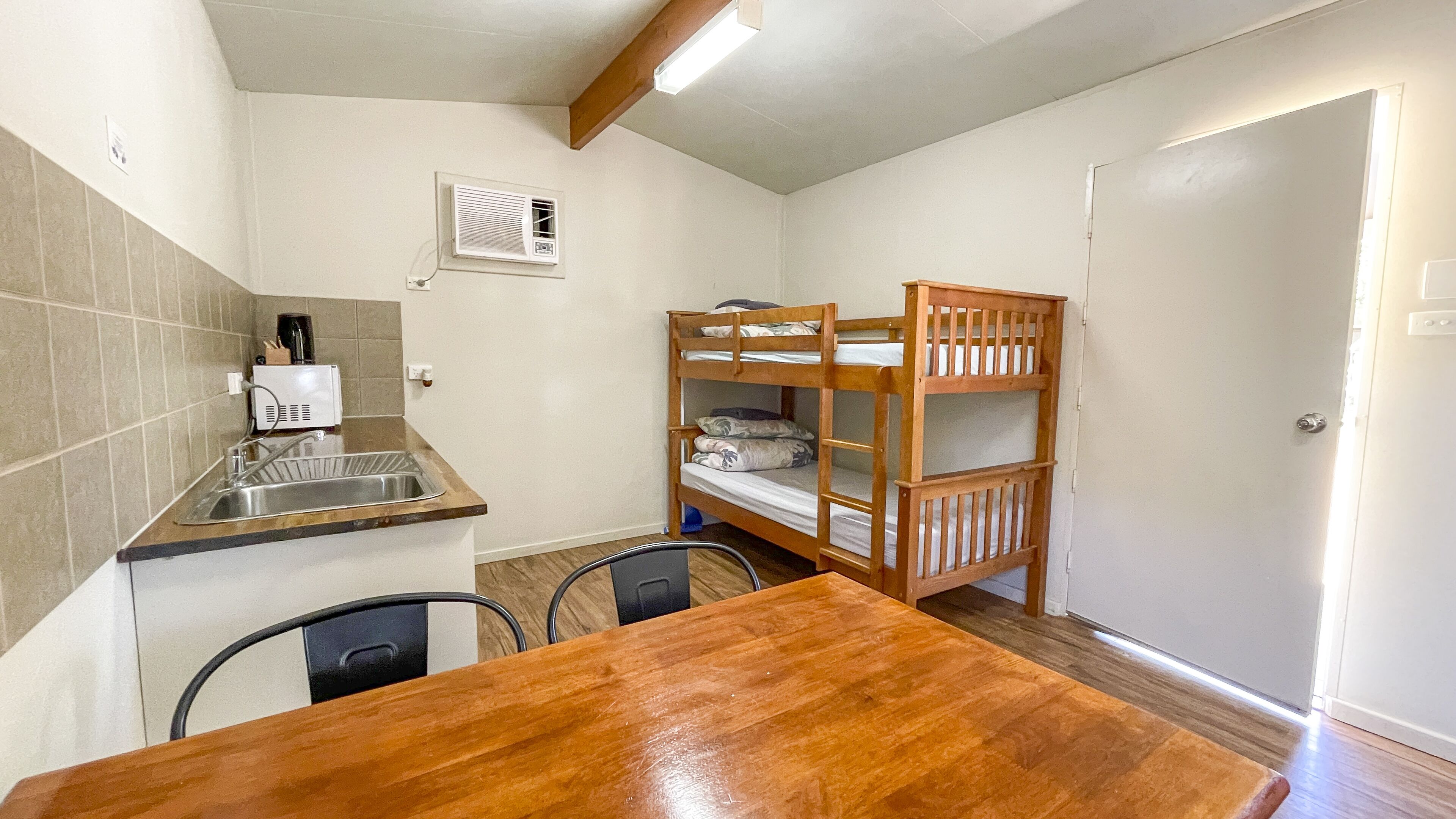 A compact kitchen with a sink, a wooden table, and a bunk bed.