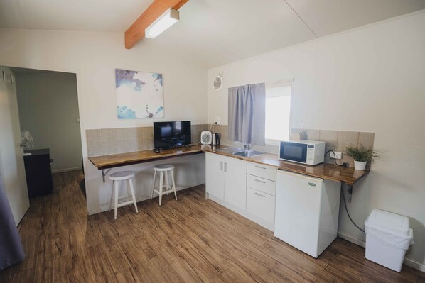 Una cocina compacta con encimera de madera, microondas, lavamanos y un refrigerador pequeño. Hay un taburete y un cuadro en la pared.