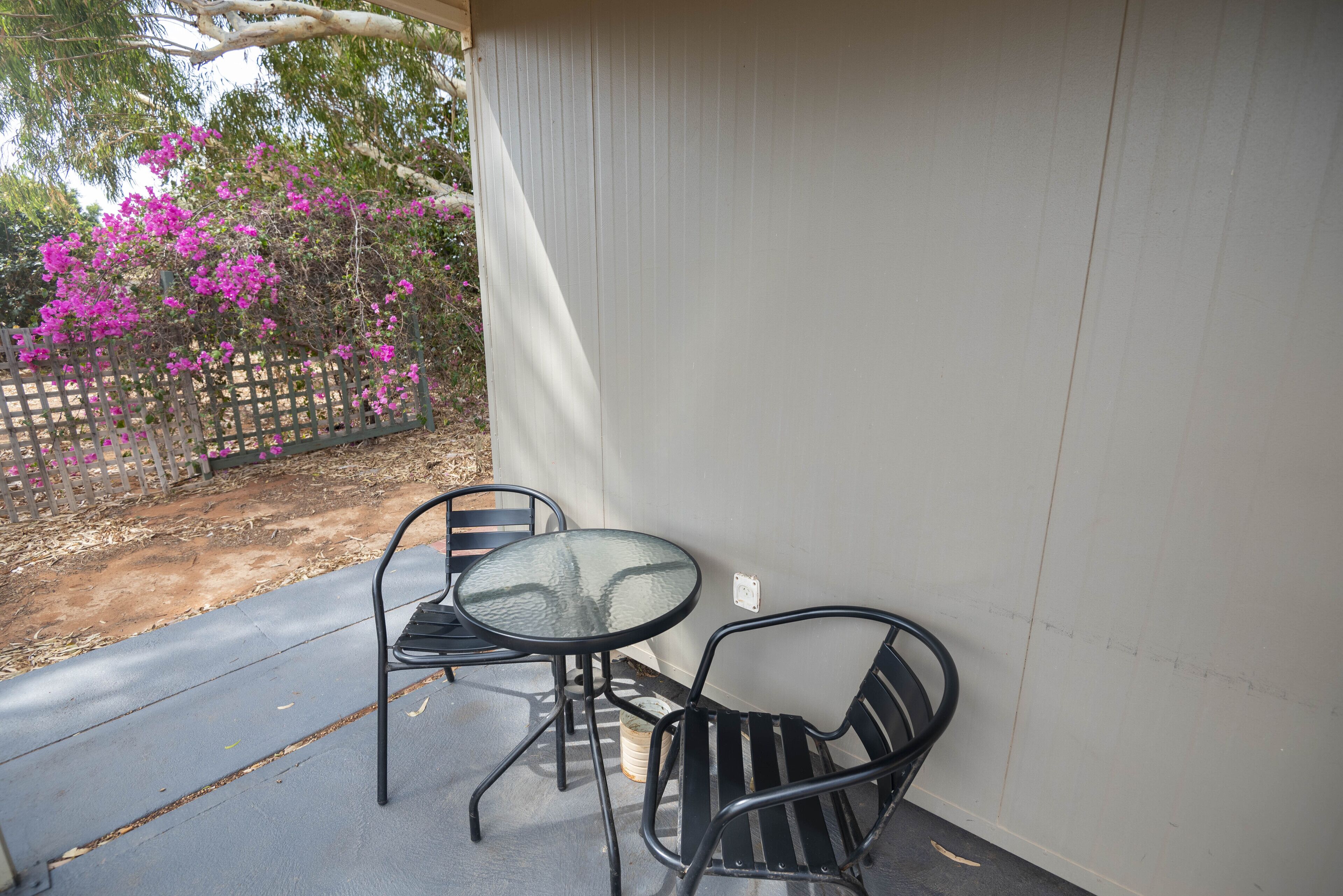 A patio with a table and two chairs, a wooden fence, and a flowering tree.