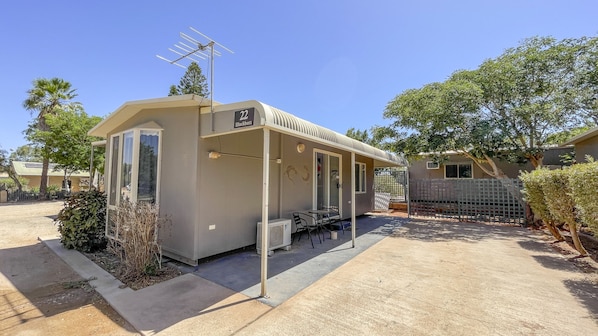 A small, single-story building with a flat roof, a covered porch, and a satellite dish.