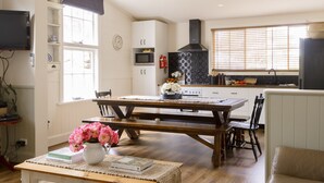 A cozy kitchen with a wooden table and chairs, a white cabinet, a black stove hood, and a window with blinds. - Freshwater Creek Cottages and Farm Stay (Freshwater Creek)