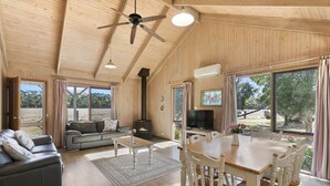 A spacious living room with a fireplace, a television, and a dining area with wooden chairs. - Freshwater Creek Cottages and Farm Stay (Freshwater Creek)