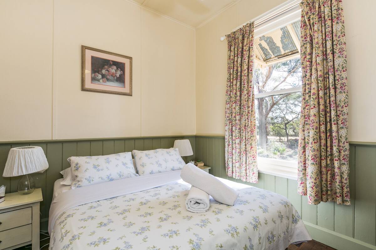 Una cama bien hecha con ropa de cama floral, una lámpara de noche y un cuadro floral enmarcado en la pared.