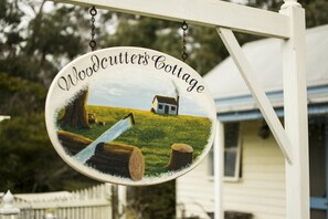 Une enseigne indiquant l’emplacement de « Woodcutters Cottage », avec une maison et des arbres en arrière-plan.