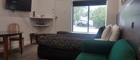 Ein Zimmer mit einem Bett, einem grünen Sofa, einem kleinen Tisch, einem an der Wand montierten Fernseher und einem Fenster mit Ausblick.