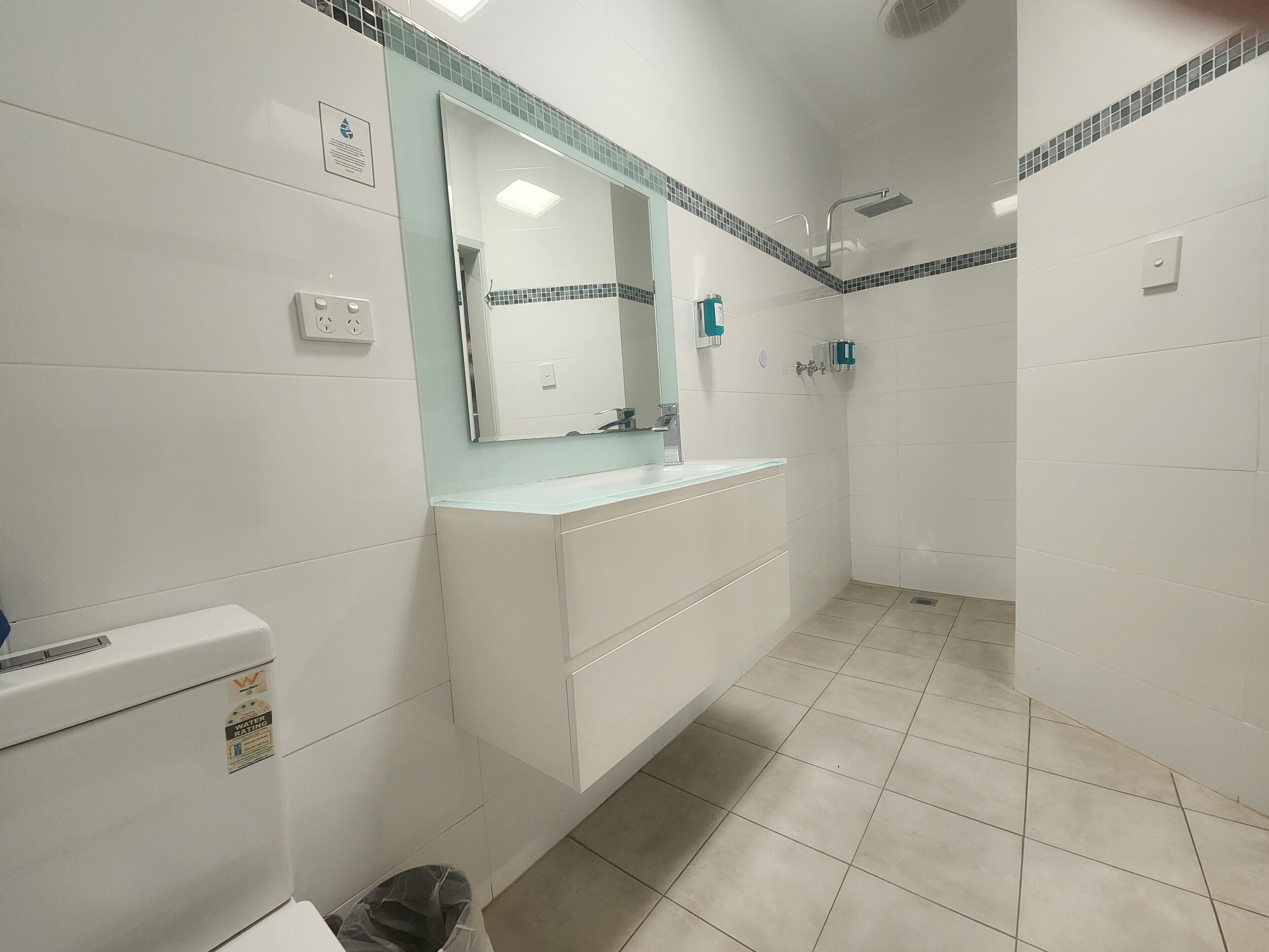 Een badkamer met een wit wastafelmeubel, een spiegel, een douche en een toilet.