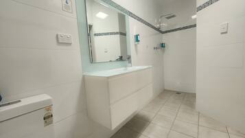 Een badkamer met een wit wastafelmeubel, een spiegel, een douche en een toilet.