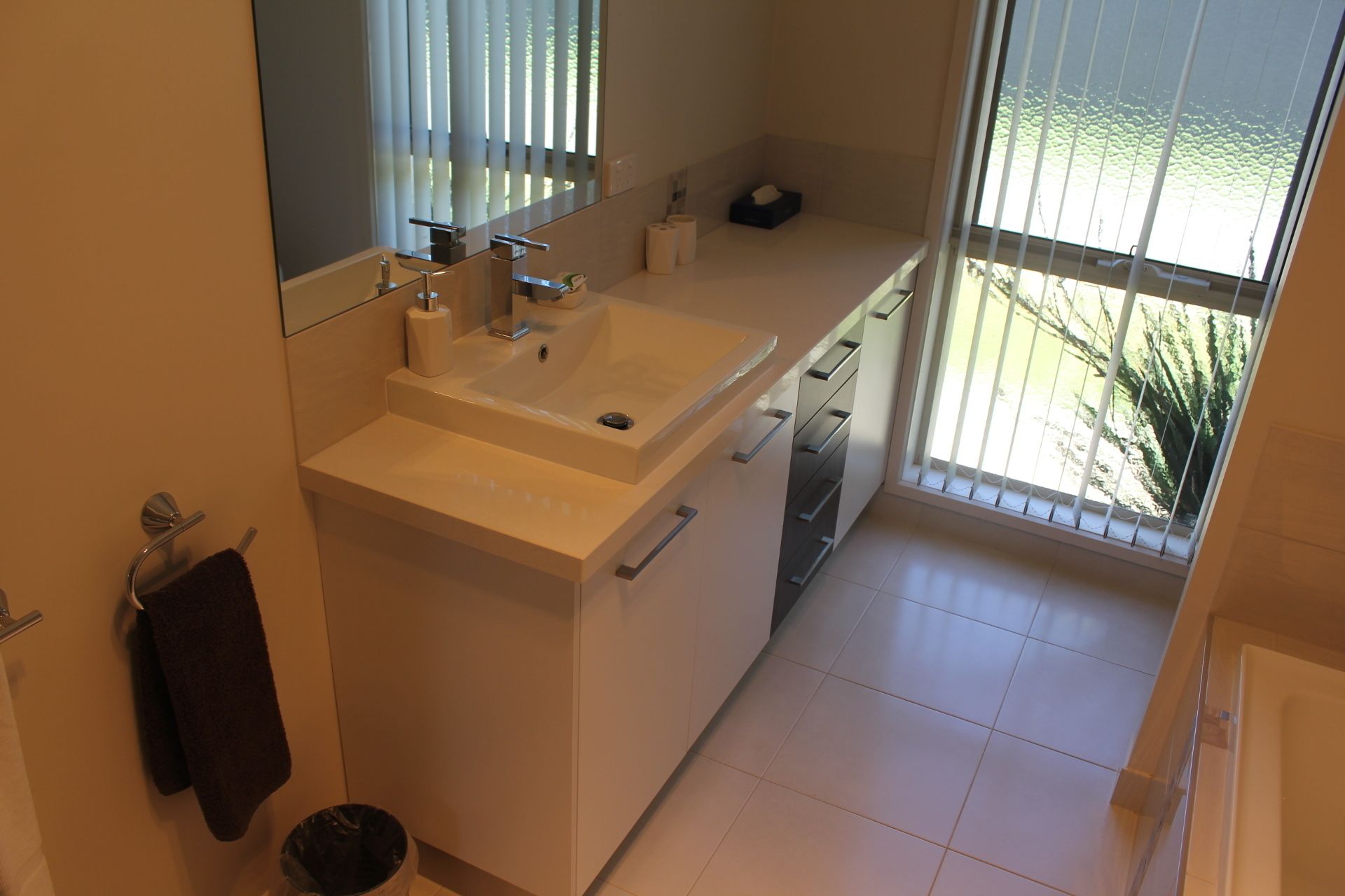 A modern bathroom with a large sink, mirror, and a view of greenery through the window.