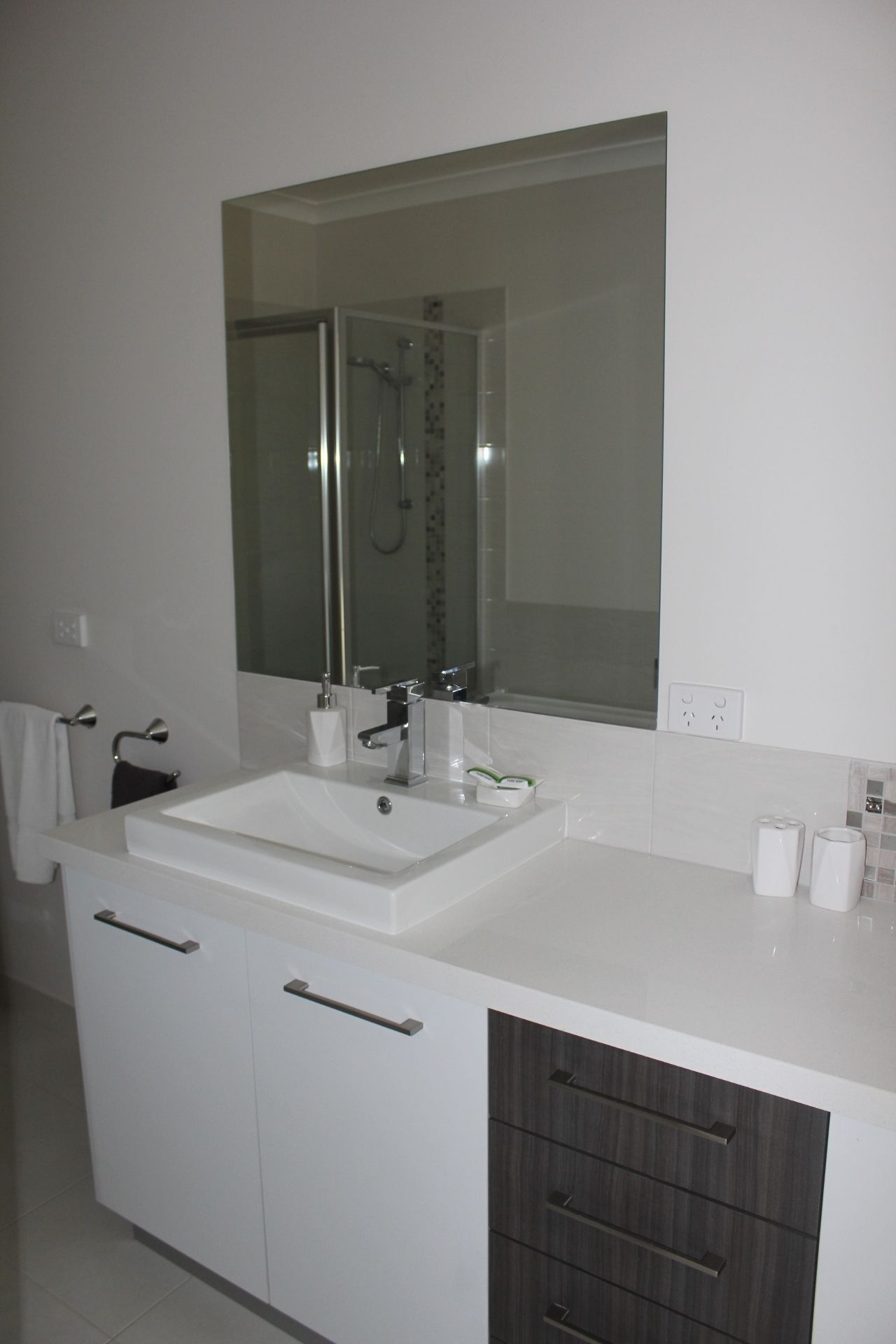 A modern bathroom with a white sink, a large mirror, and a shower enclosure.