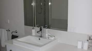 A modern bathroom with a white sink, a large mirror, and a shower enclosure.