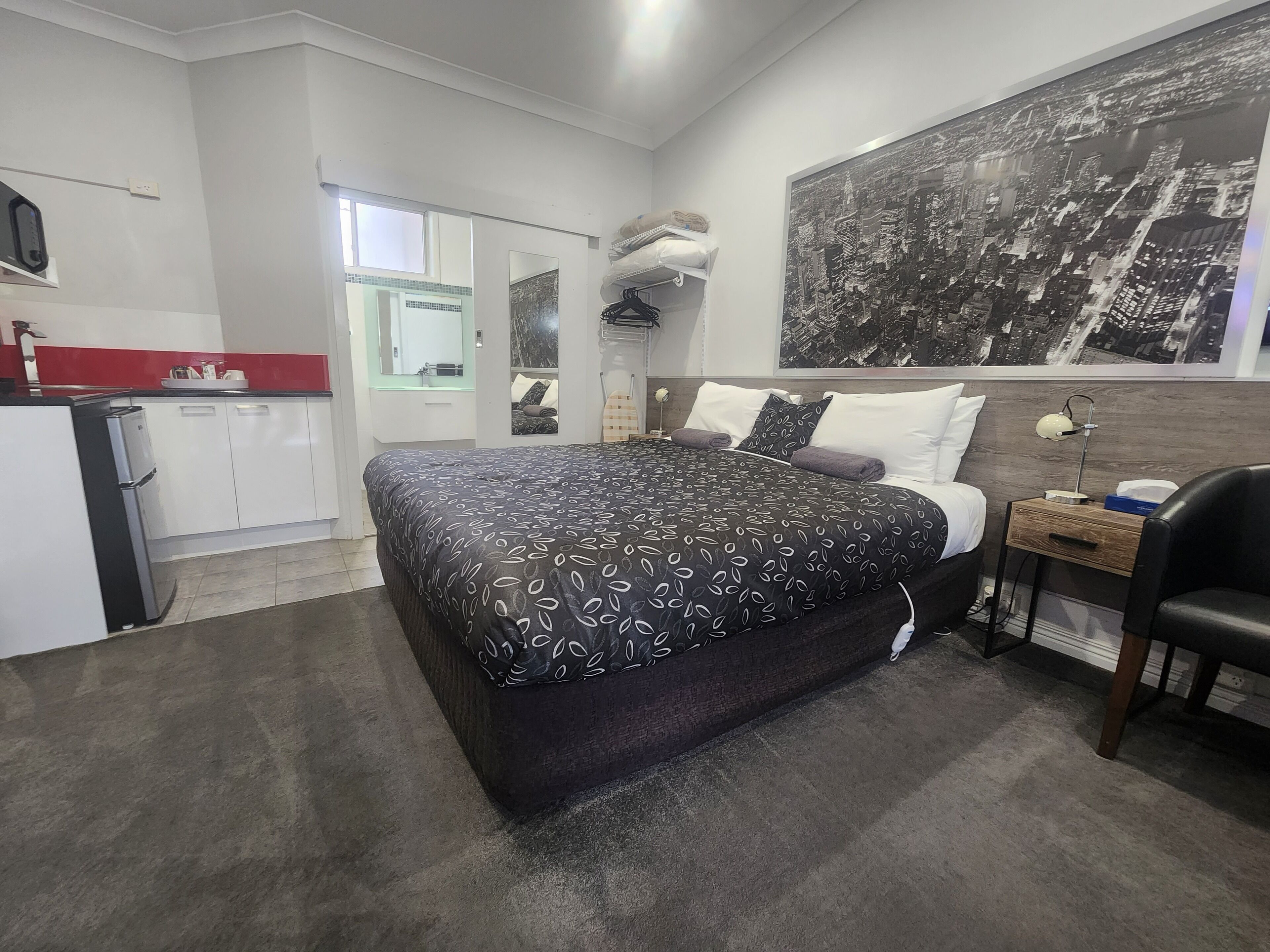 Une chambre d’hôtel moderne dotée d’un grand lit, d’un bureau, d  ’une chaise, d’une armoire et d’une fresque murale représentant un paysage urbain.