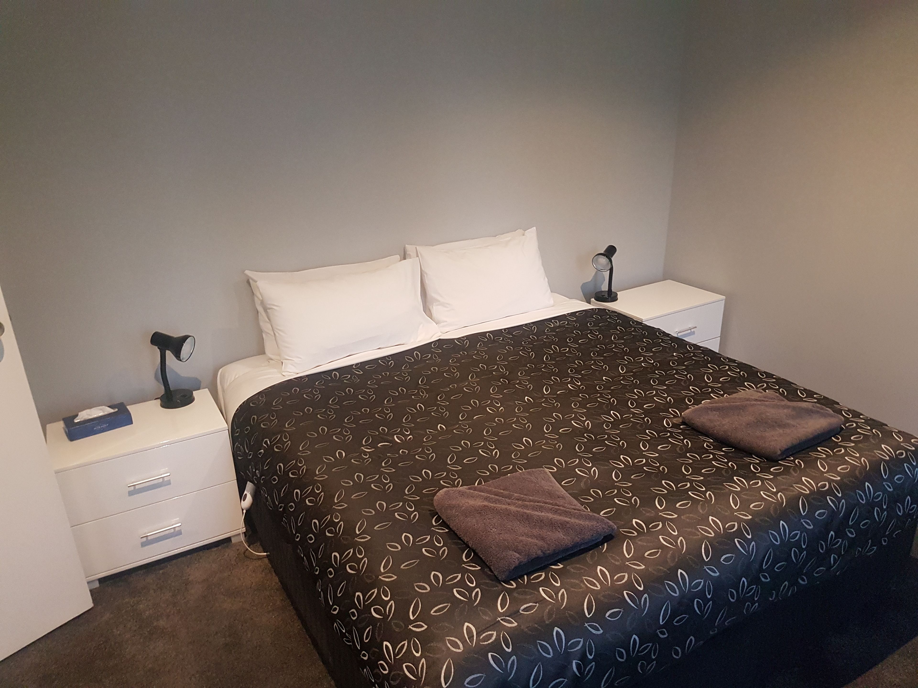 A neatly made bed with a patterned bedspread, two pillows, and two bedside lamps on white nightstands.
