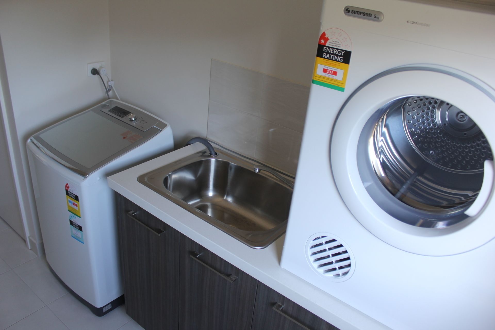 Un espace réduit dédié à la buanderie, comprenant un lave-linge, un petit sèche-linge et un évier.