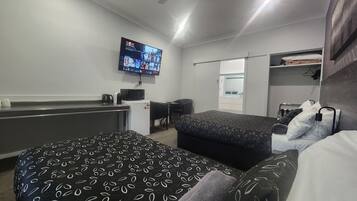 Habitación de hotel con dos camas, un escritorio, microondas, refrigerador, televisor mostrando un canal de deportes y ventilador de techo.