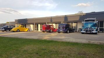 A parking lot with vintage cars and a large truck in front of a building with a flat roof and large windows.
