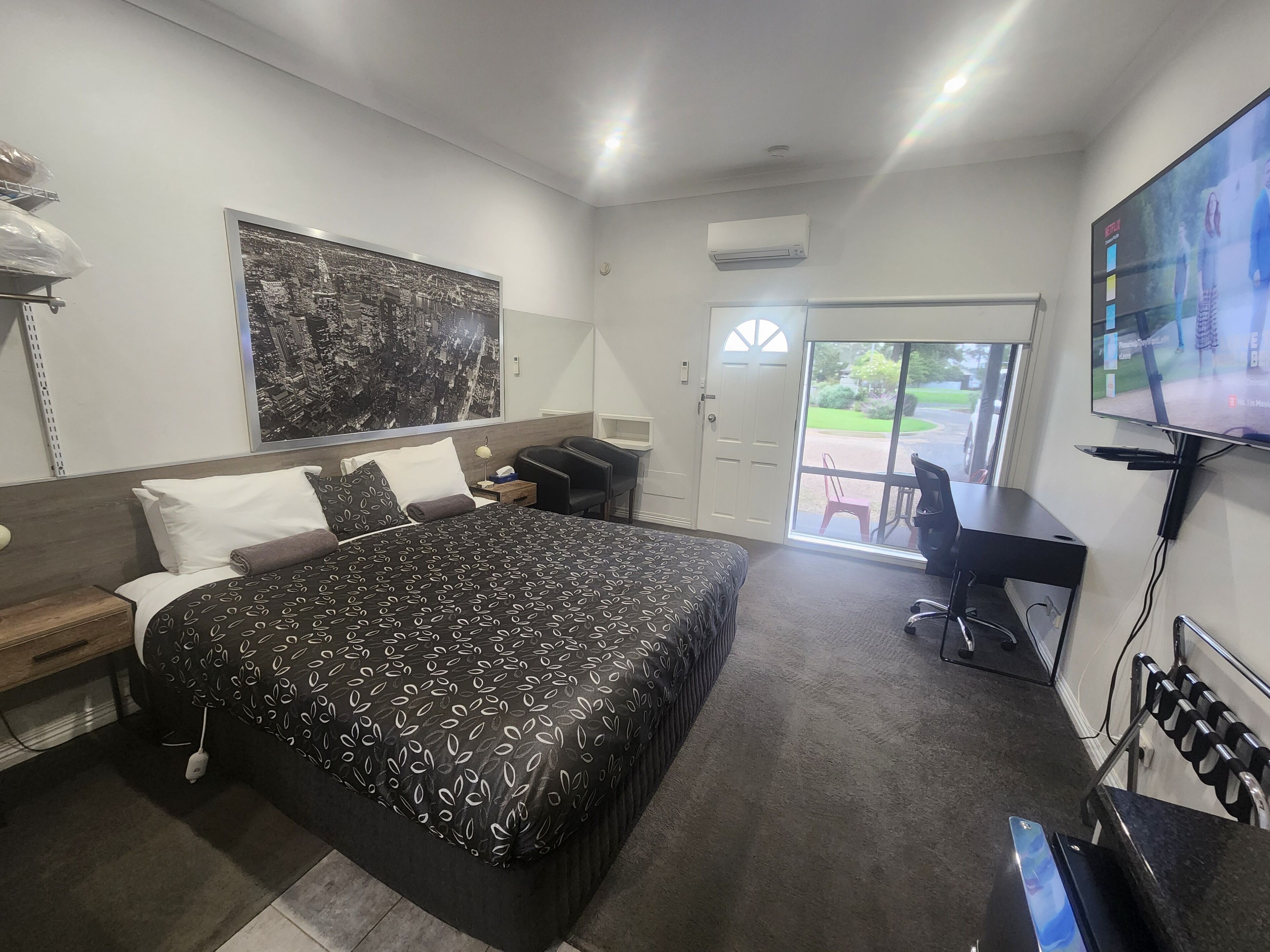 A hotel room with a large bed, a desk, a chair, a TV, and a door leading to a balcony.