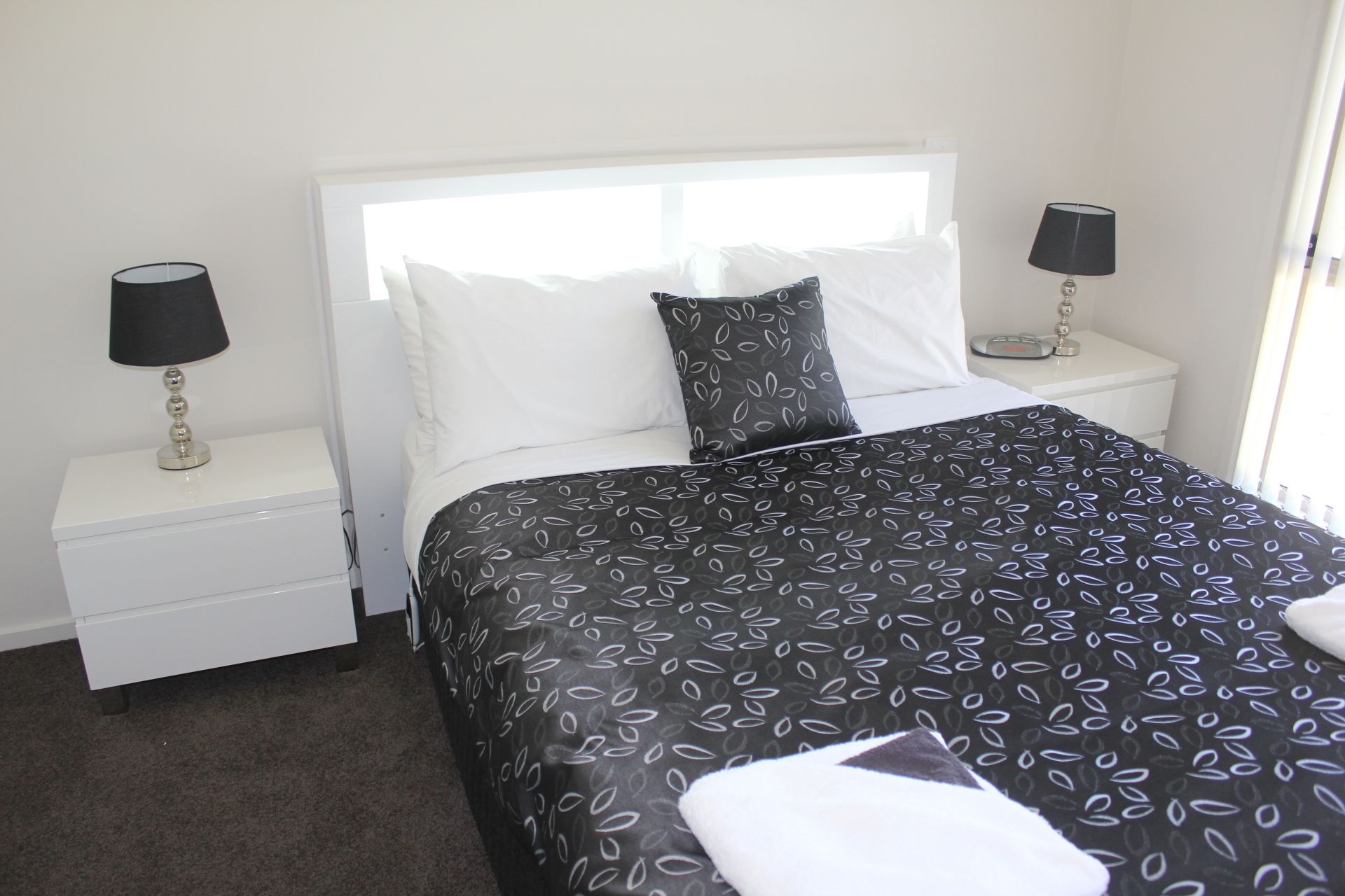 A hotel room with a bed, white nightstands, two lamps, and a window.
