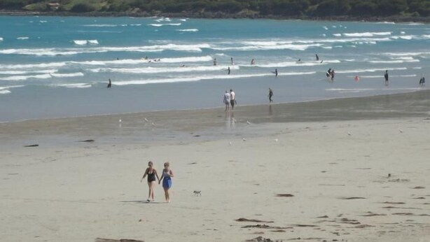 Una playa con gente caminando y practicando surf.