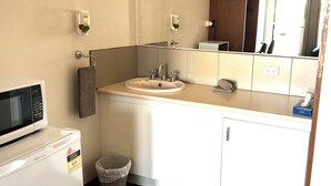 Un baño con lavamanos, espejo, toallero, cubo de basura y microondas.