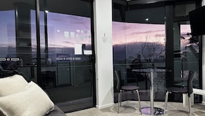 Una sala de estar moderna con un ventanal que da a un balcón, un comedor con sillas y un sofá con cojín.