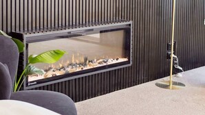 Una sala de estar moderna con un televisor de pantalla plana montado en una pared de madera oscura, una chimenea con frente de vidrio y una lámpara de pie.