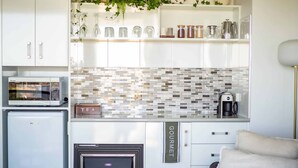 Cocina compacta equipada con microondas, tostadora y cafetera. Incluye un refrigerador pequeño, horno empotrado y un estante con frascos y una caja de té.
