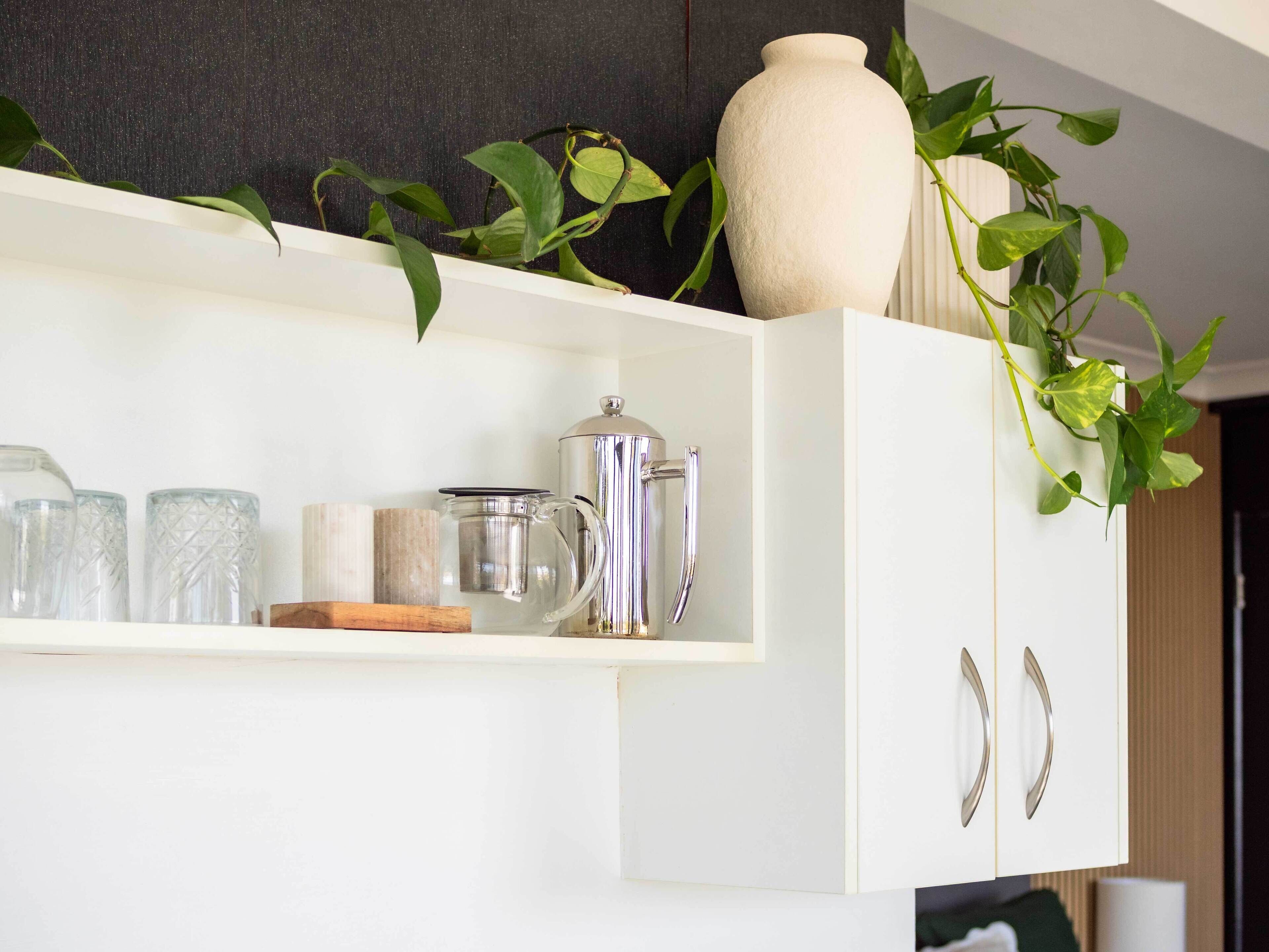 A white shelf with a coffee maker, glass jars, and a vase with green plants.