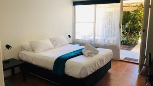 Une chambre à coucher avec un lit, une table de chevet, une fenêtre avec des rideaux et une vue sur la verdure à l’extérieur.