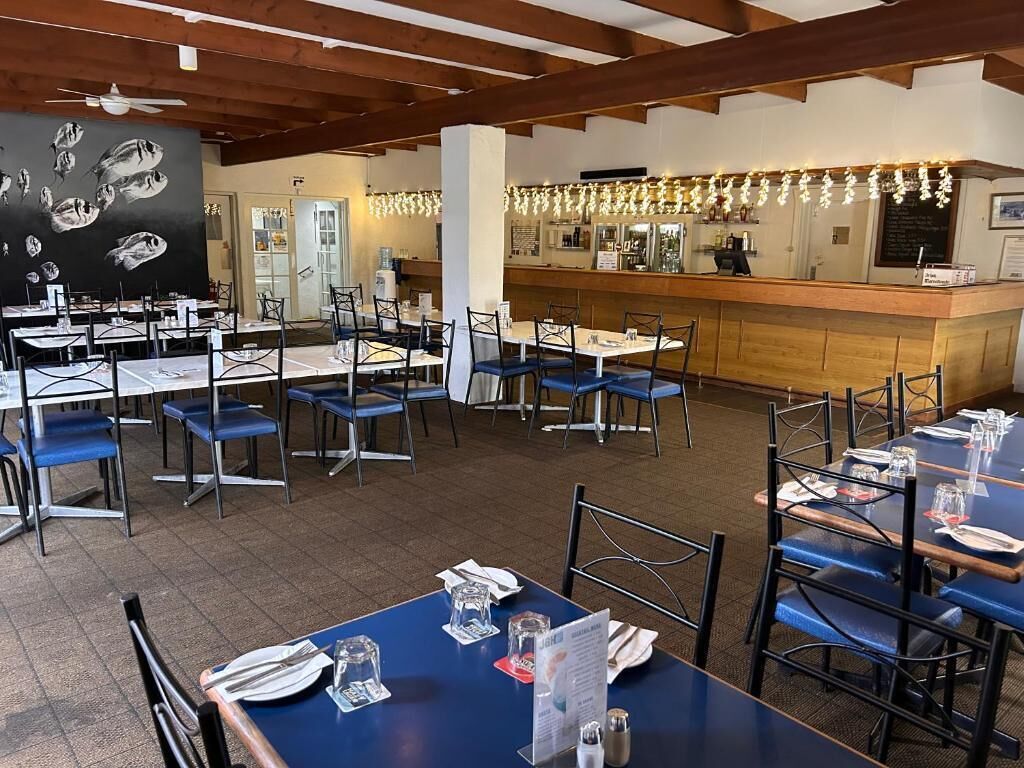 A restaurant with multiple tables and chairs, a bar area, and a blackboard with fish illustrations.