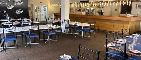 A restaurant with multiple tables and chairs, a bar area, and a blackboard with fish illustrations.