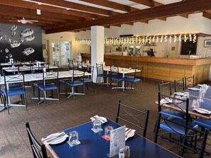 Un restaurant doté de nombreuses tables et chaises, d’un bar et d’un tableau noir orné d’illustrations de poissons.