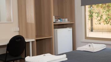 A bedroom with a bed, a desk, a chair, a wardrobe, and a window with a view of greenery.