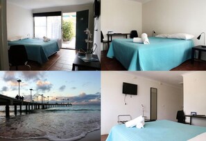 Hotelkamer met twee bedden, een bureau, een stoel, een televisie en uitzicht op het strand en de pier.