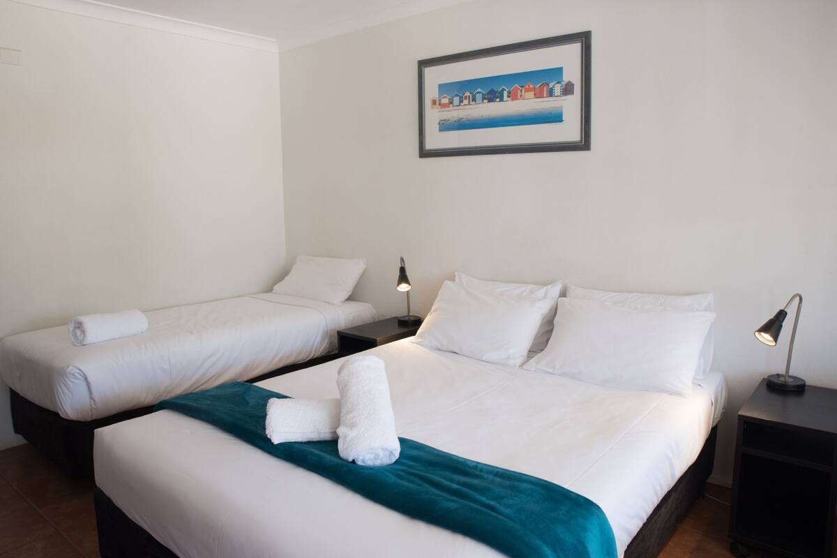 Habitación de hotel con dos camas, ropa de cama blanca, mantas color turquesa y un cuadro en la pared.